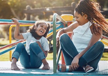 mom and daughter playing on carousel at playground